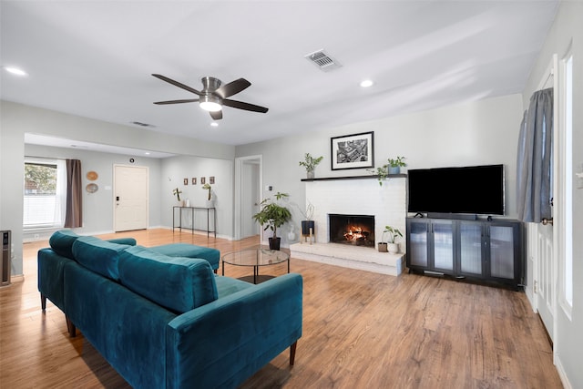 living room with hardwood / wood-style floors, ceiling fan, and a brick fireplace