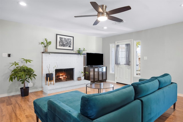 living room with a brick fireplace, wood-type flooring, and ceiling fan