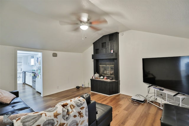 living room with wood-type flooring, a textured ceiling, vaulted ceiling, a large fireplace, and ceiling fan