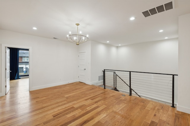 spare room featuring a chandelier and light hardwood / wood-style flooring