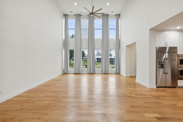 unfurnished living room with a high ceiling, ceiling fan, and light hardwood / wood-style flooring