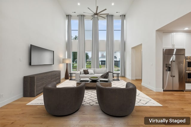 living room featuring a towering ceiling, ceiling fan, and light wood-type flooring