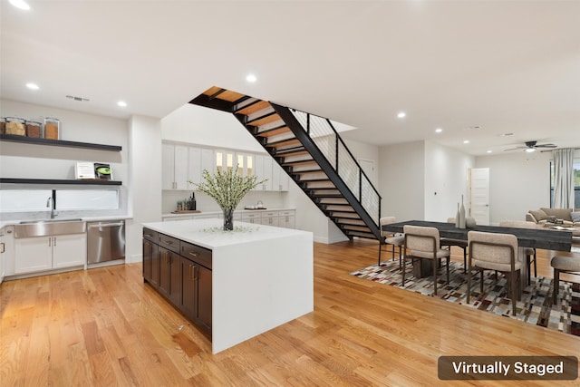 kitchen with a center island, sink, stainless steel dishwasher, white cabinetry, and light hardwood / wood-style flooring