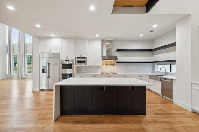 kitchen featuring sink, appliances with stainless steel finishes, wall chimney exhaust hood, light hardwood / wood-style flooring, and a center island