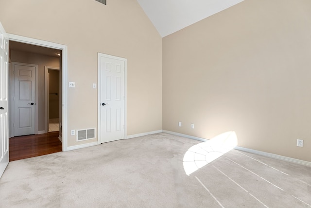 unfurnished bedroom with high vaulted ceiling and light colored carpet