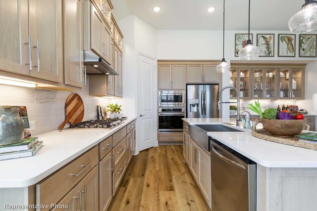 kitchen with a center island with sink, sink, appliances with stainless steel finishes, decorative light fixtures, and light hardwood / wood-style flooring