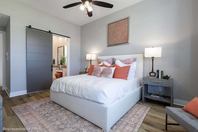 bedroom with ensuite bathroom, a barn door, ceiling fan, and wood-type flooring