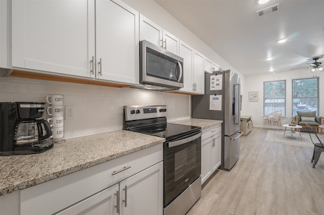 kitchen featuring tasteful backsplash, white cabinetry, appliances with stainless steel finishes, light wood-type flooring, and light stone countertops