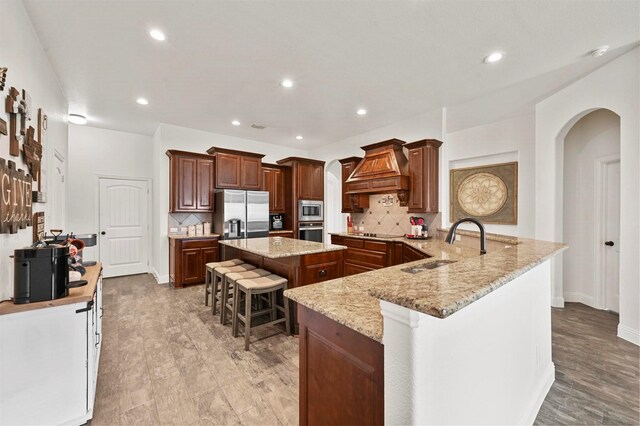 kitchen with sink, a breakfast bar area, kitchen peninsula, custom range hood, and stainless steel appliances