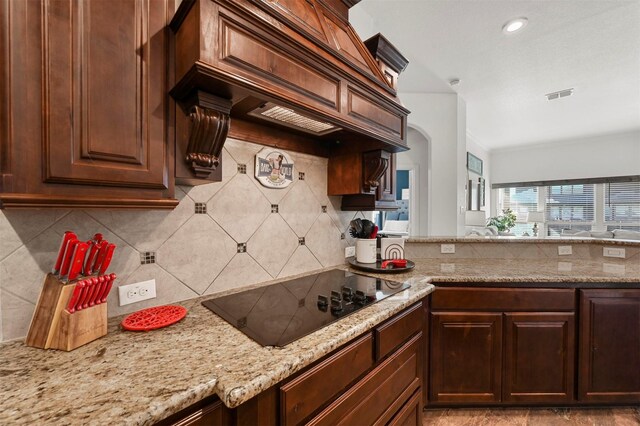 kitchen with sink, a kitchen breakfast bar, light stone counters, black electric stovetop, and a kitchen island