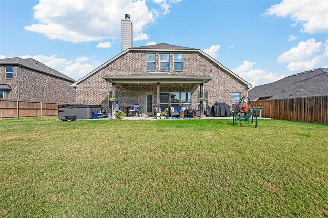 rear view of property featuring a yard, a patio area, and a hot tub