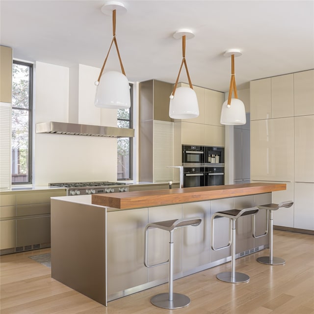 kitchen featuring light hardwood / wood-style floors, a breakfast bar area, stainless steel range, wood counters, and decorative light fixtures