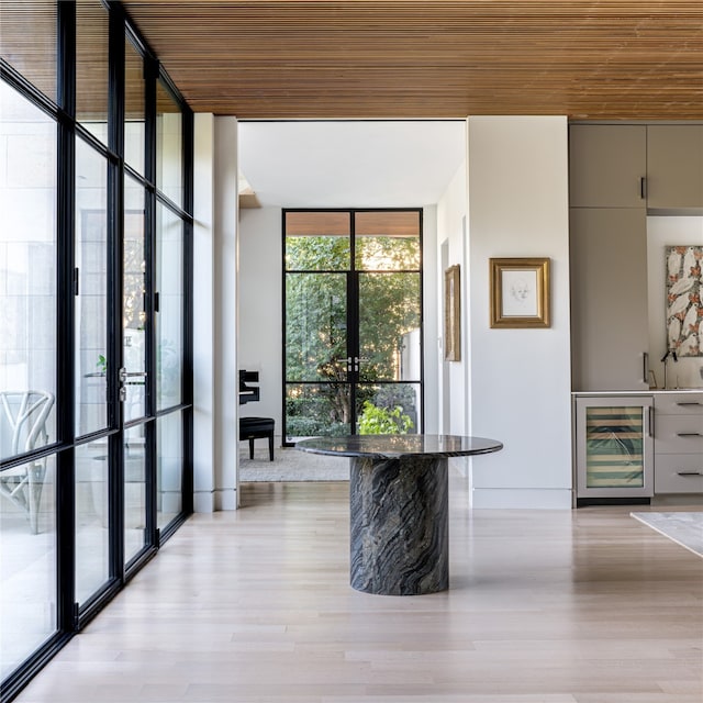 interior space with beverage cooler, a wall of windows, french doors, and light hardwood / wood-style flooring