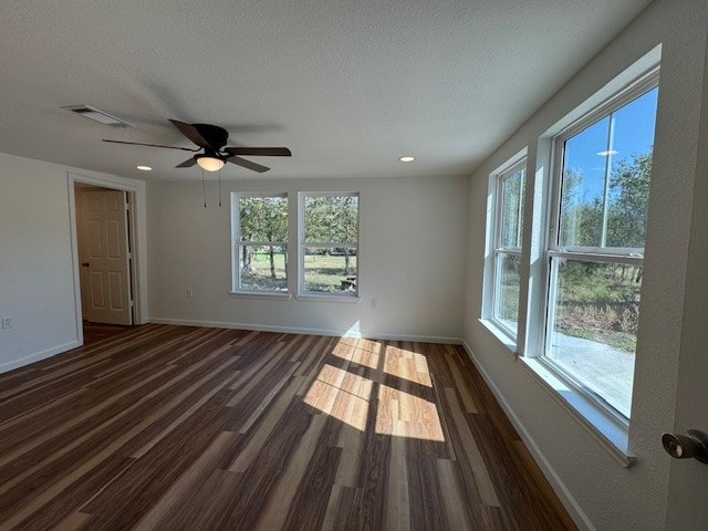 spare room with dark wood-type flooring, ceiling fan, a textured ceiling, and a healthy amount of sunlight