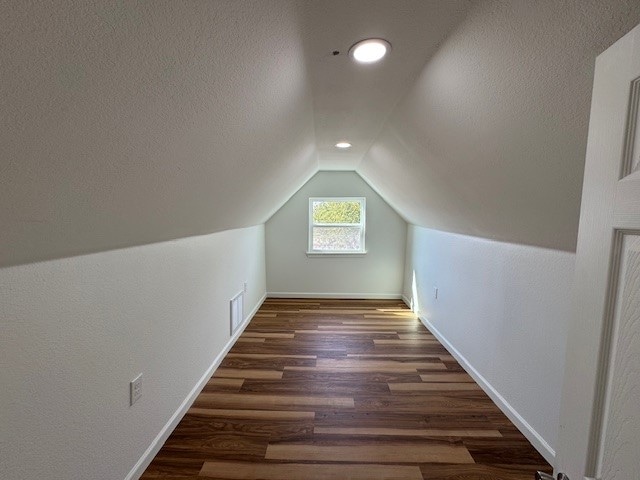 bonus room featuring dark hardwood / wood-style flooring, a textured ceiling, and vaulted ceiling