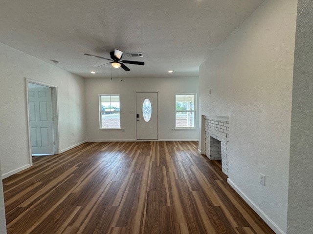 unfurnished living room with ceiling fan, dark hardwood / wood-style floors, a healthy amount of sunlight, and a brick fireplace