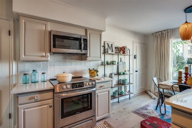 kitchen featuring light wood-type flooring, appliances with stainless steel finishes, backsplash, and hanging light fixtures