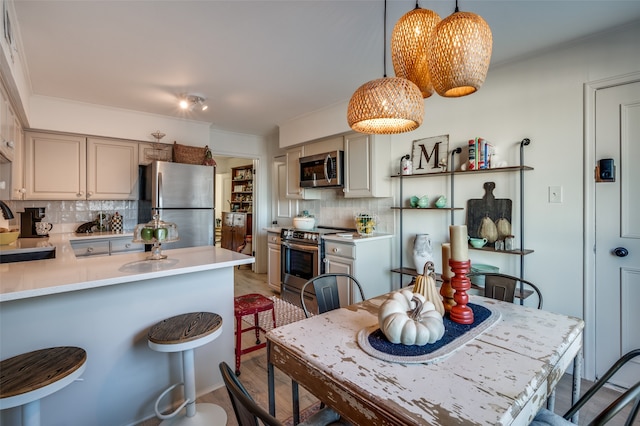 kitchen with a kitchen bar, decorative backsplash, appliances with stainless steel finishes, and hanging light fixtures