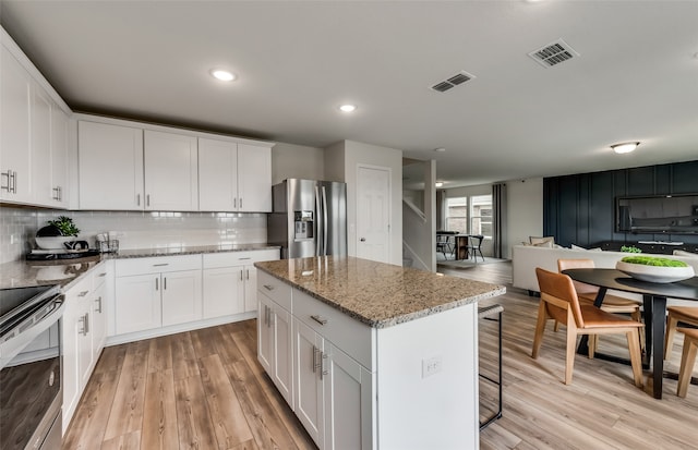 kitchen with light stone counters, stainless steel appliances, white cabinets, light hardwood / wood-style floors, and a kitchen island