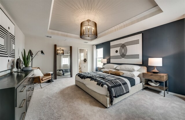 bedroom featuring light carpet, a tray ceiling, a chandelier, and ensuite bathroom