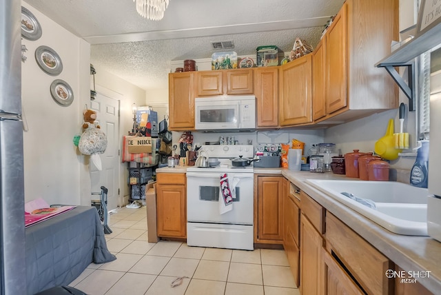 kitchen featuring white appliances, sink, light tile patterned floors, and a textured ceiling