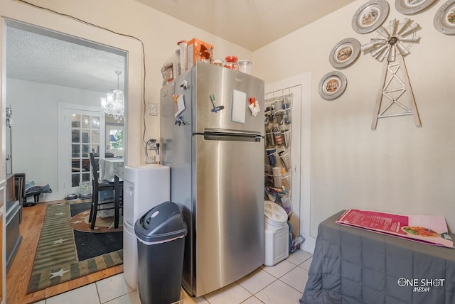 kitchen featuring a textured ceiling, stainless steel refrigerator, light tile patterned floors, and an inviting chandelier