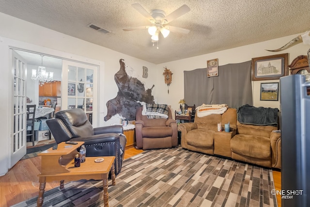 living room with ceiling fan with notable chandelier, french doors, light hardwood / wood-style floors, and a textured ceiling