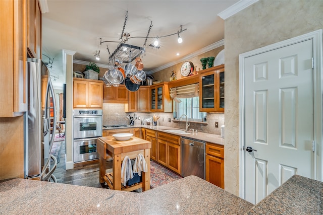 kitchen with ornamental molding, appliances with stainless steel finishes, dark hardwood / wood-style flooring, sink, and dark stone countertops