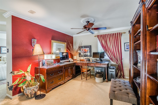 carpeted office space with built in desk, ceiling fan, and crown molding