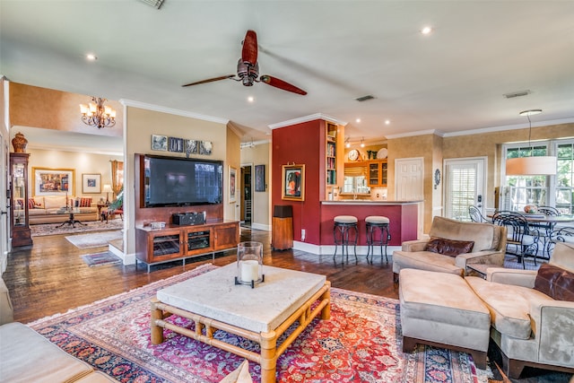 living room with ceiling fan with notable chandelier, dark wood-type flooring, and crown molding