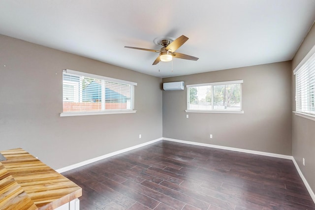 empty room featuring a wall unit AC, plenty of natural light, dark wood-type flooring, and ceiling fan