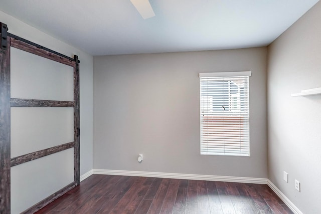 spare room featuring ceiling fan, a barn door, and dark hardwood / wood-style floors