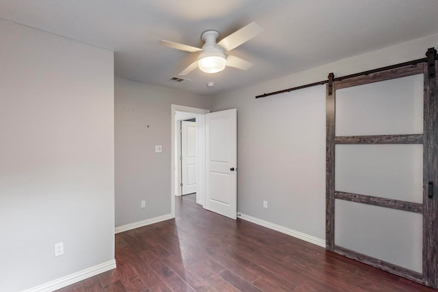 unfurnished bedroom featuring a barn door, ceiling fan, and dark hardwood / wood-style floors