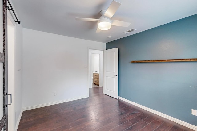 empty room featuring dark wood-type flooring, a barn door, and ceiling fan