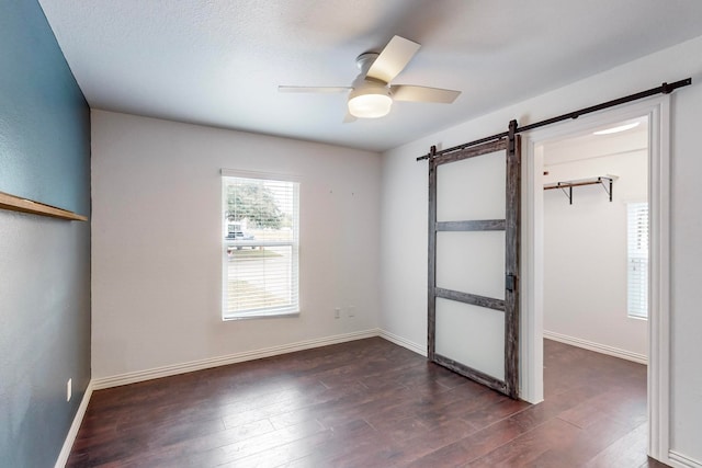 unfurnished bedroom with a barn door, ceiling fan, and dark hardwood / wood-style floors