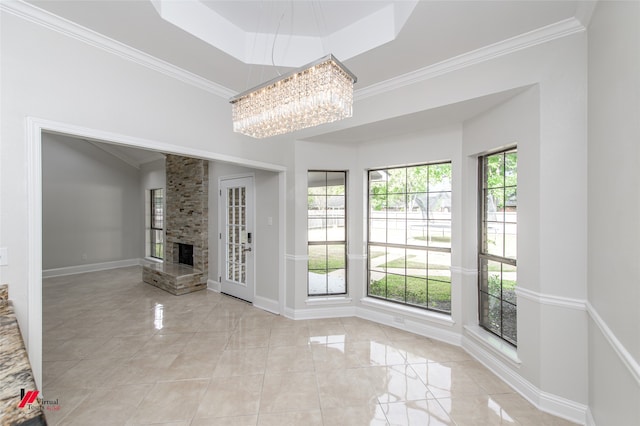 unfurnished living room featuring a fireplace, a raised ceiling, an inviting chandelier, and crown molding