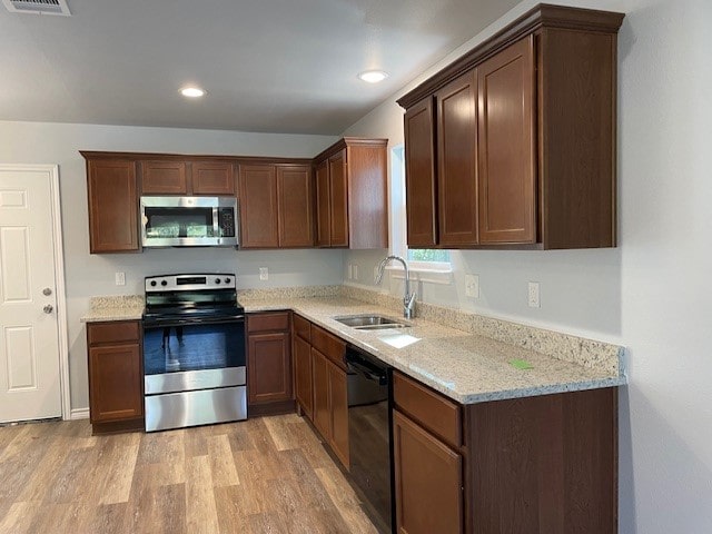 kitchen with light hardwood / wood-style floors, appliances with stainless steel finishes, sink, and light stone countertops