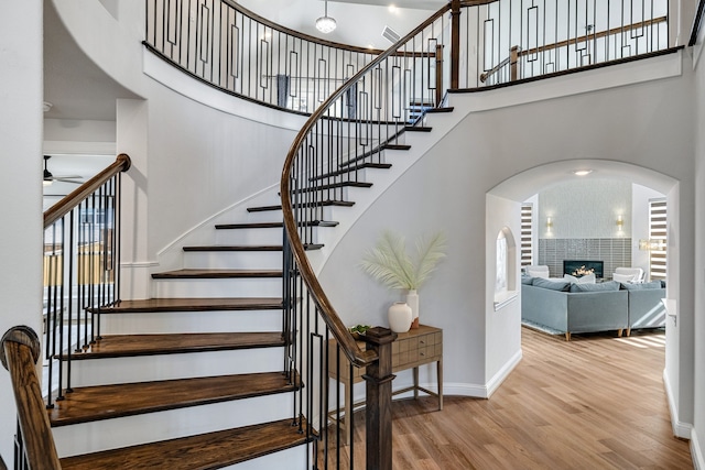 staircase featuring a towering ceiling, hardwood / wood-style floors, and a tiled fireplace