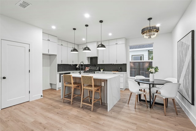 kitchen with light hardwood / wood-style floors, a center island with sink, white cabinets, hanging light fixtures, and backsplash