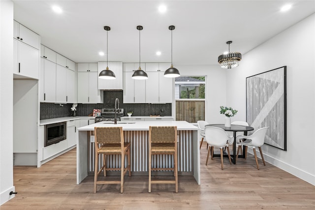 kitchen featuring white cabinets, decorative light fixtures, and light wood-type flooring