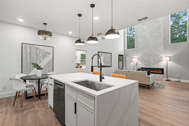 kitchen with a fireplace, decorative light fixtures, sink, white cabinets, and a kitchen island with sink