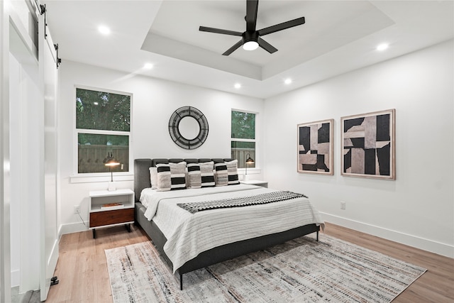 bedroom with a tray ceiling, multiple windows, hardwood / wood-style flooring, and ceiling fan