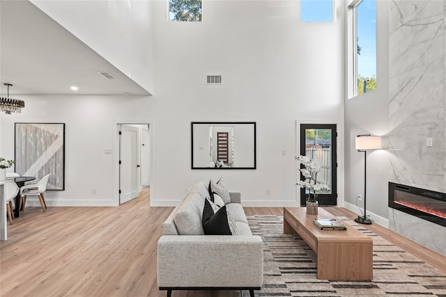 living room featuring a tiled fireplace, a towering ceiling, and light hardwood / wood-style floors