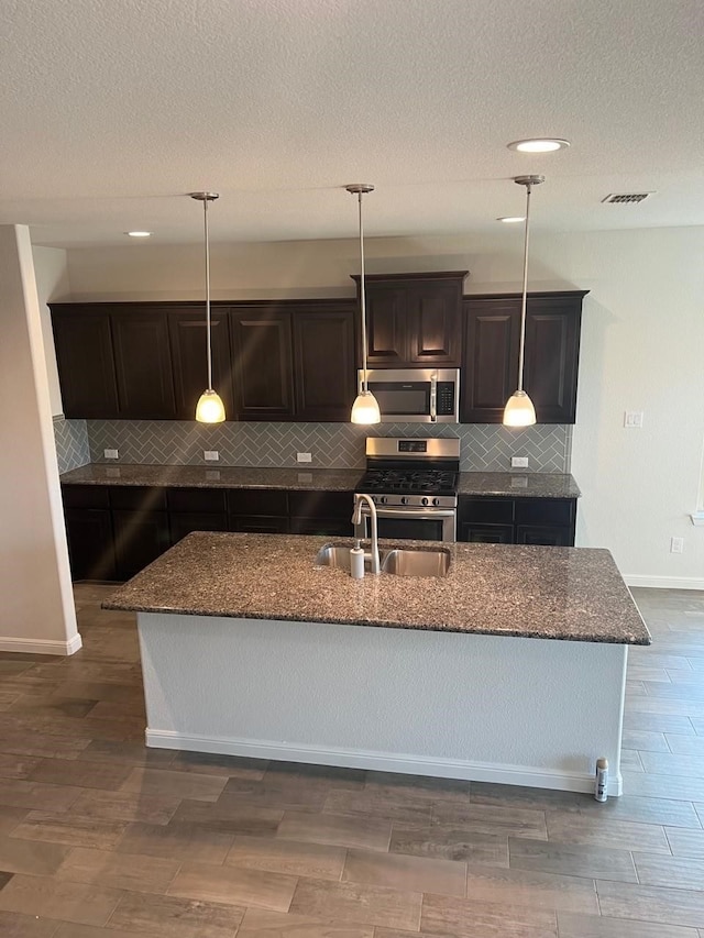 kitchen featuring an island with sink, dark hardwood / wood-style floors, stainless steel appliances, and tasteful backsplash