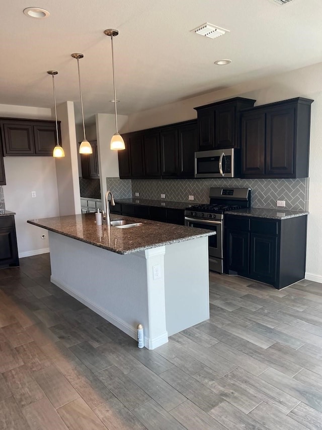 kitchen featuring a kitchen island with sink, stainless steel appliances, hanging light fixtures, sink, and light hardwood / wood-style flooring