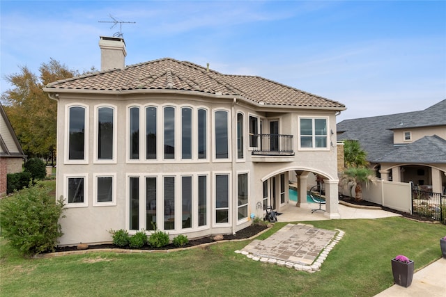 rear view of house featuring a lawn, a balcony, and a patio