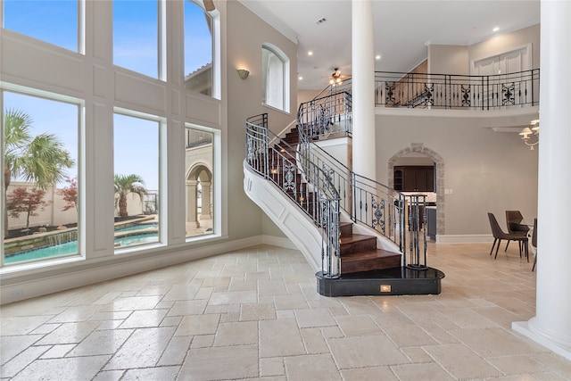 stairway with ornamental molding, a towering ceiling, and plenty of natural light