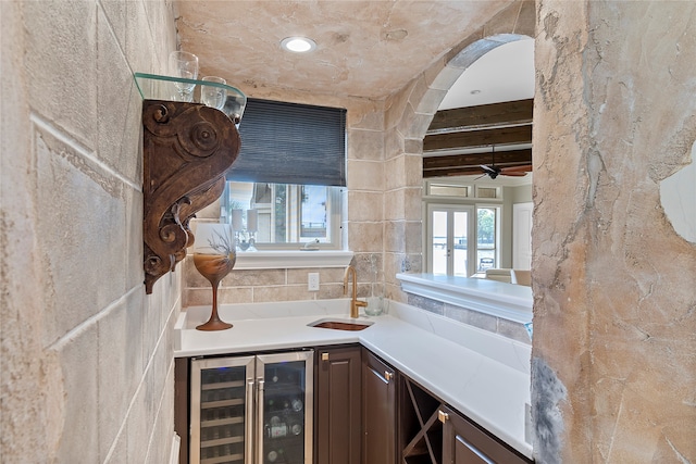 bar with dark brown cabinetry, beam ceiling, wine cooler, and sink