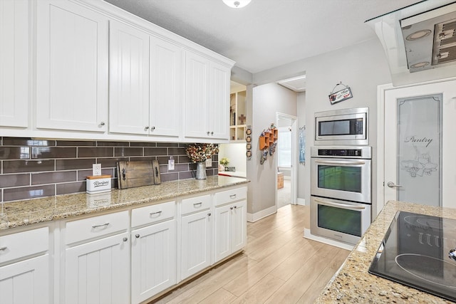 kitchen featuring tasteful backsplash, light stone counters, white cabinetry, appliances with stainless steel finishes, and light hardwood / wood-style floors