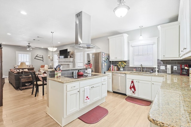 kitchen featuring stainless steel appliances, island range hood, white cabinets, sink, and decorative light fixtures